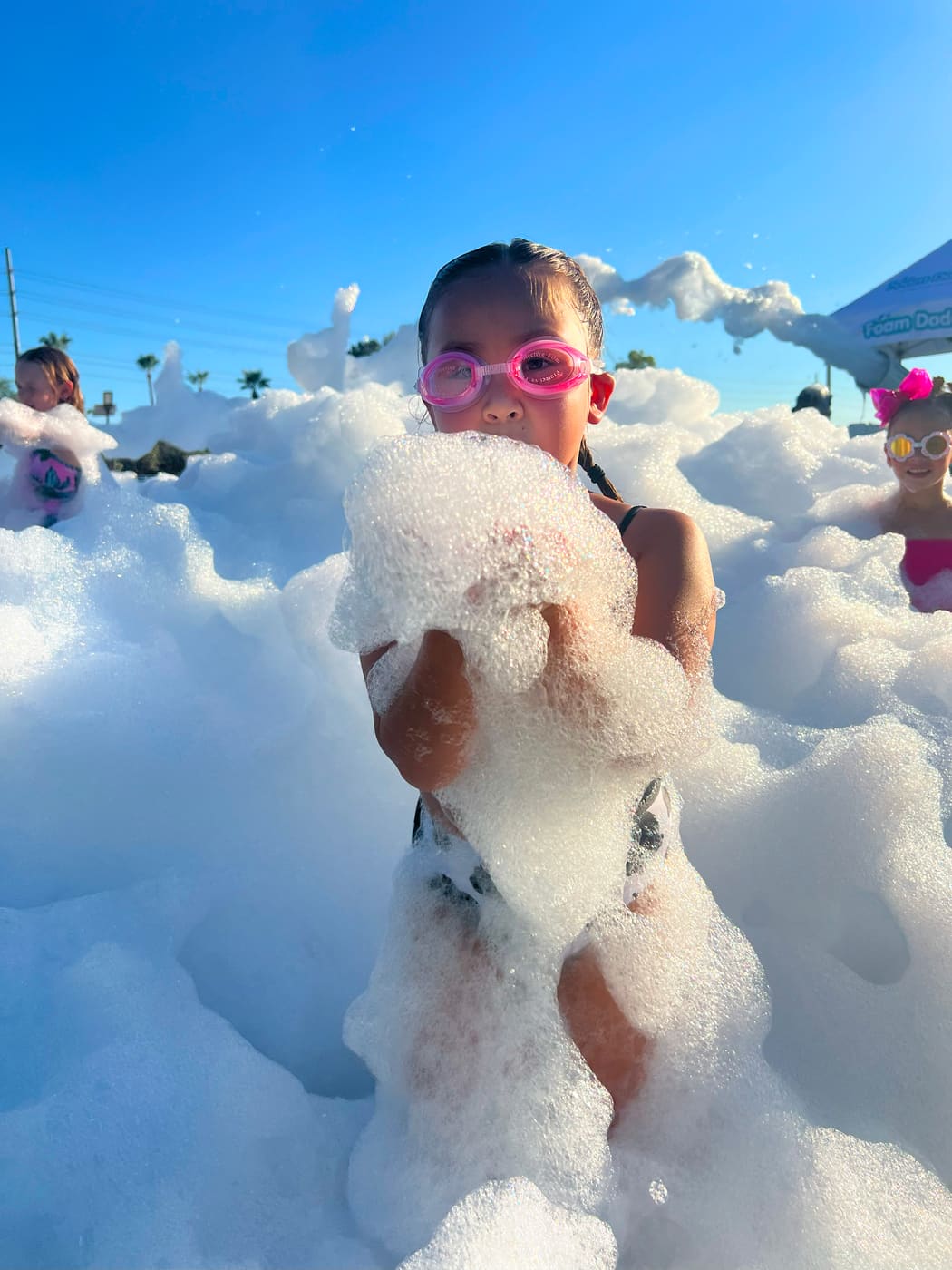 A girl in pink goggles holding up a handful of foam